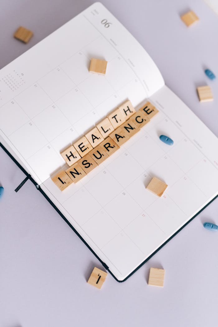 Flat lay of planner with Health Insurance in Scrabble tiles, emphasizing planning and health.